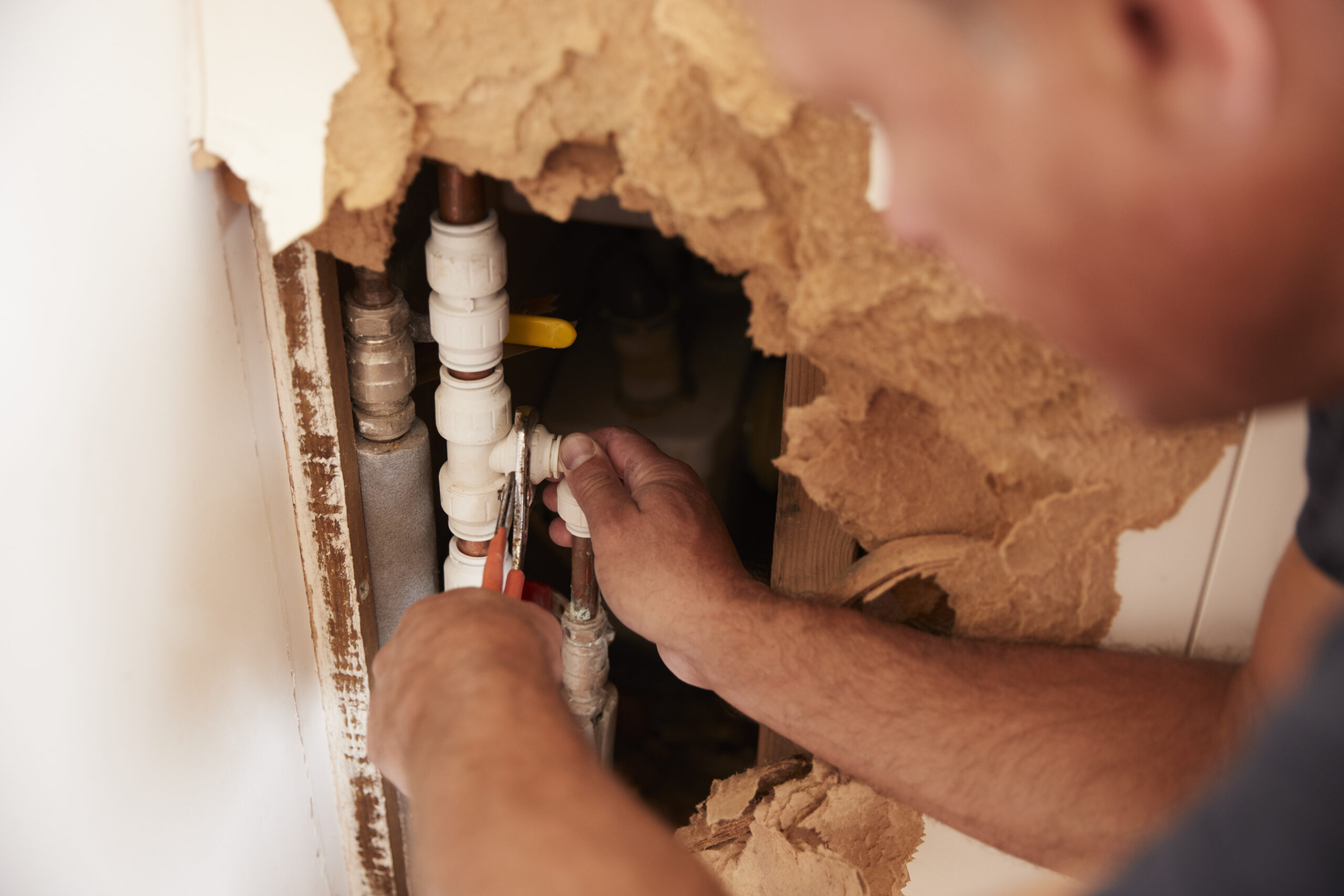 Plumber repairing a pipe inside an opened wall