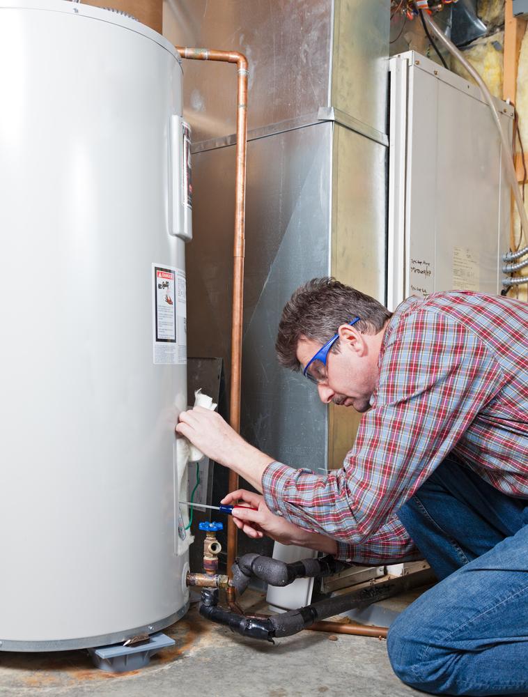 Technician inspecting plumbing beside a water heater with a flashlight